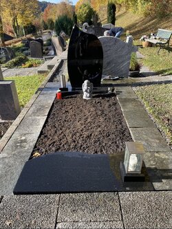 Stehender Sein hergestellt aus dunklem Granit mit teilweise abdeckender Grabplatte aus dunklem Granit  | © Messerschmidt GmbH