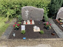 Stehender Stein hergestellt aus Granit mit weißem, eingefrästem Kreuz, welches von Rosen umringt wird  | © Messerschmidt GmbH