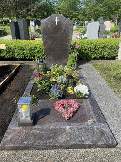 Stehender Stein hergestellt aus Granit verziert mit eingefrästen, weißen Kreuz und umrandet von einer gleichfarbigen Granit Einfassung und Grabplatte, die teils das Grab überdeckt  | © Messerschmidt GmbH  