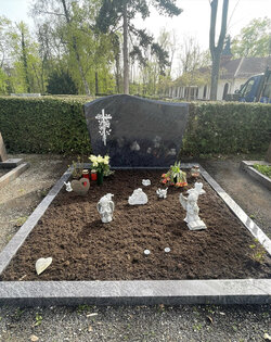 Stehender Stein hergestellt aus dunklem Granit mit weißem, eingefrästen Kreuz umgeben von Blumen umrandet von einer dunklen Granit Einfassung  | © Messerschmidt GmbH