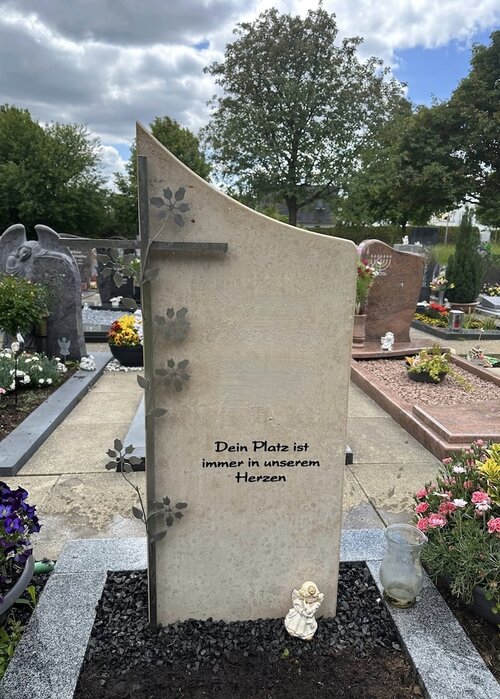 Einzelgrabstein Modell Freiburg angefertigt aus Jura Kalkstein. Dekoratives Edelstahl Element zeigt ein Kreuz mit Blattwerk. In den Stein wurde ein Spruch vertieft eingarbeitet. | © Messerschmidt GmbH